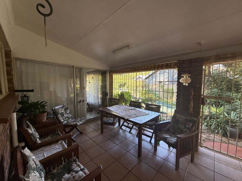 A covered patio area featuring tiled flooring, exposed brick walls, and large sliding glass doors providing access to the garden.