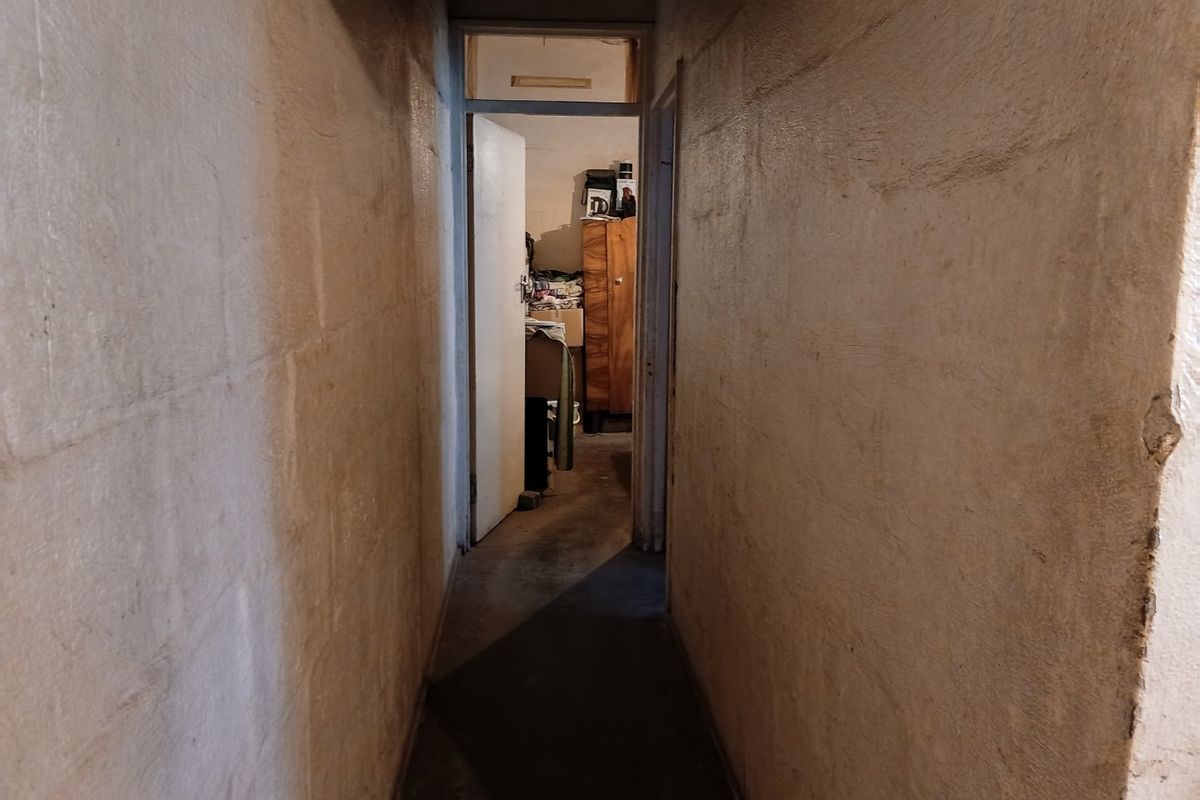 A narrow, unfinished hallway featuring exposed concrete block walls and concrete flooring, leading to an adjacent room.