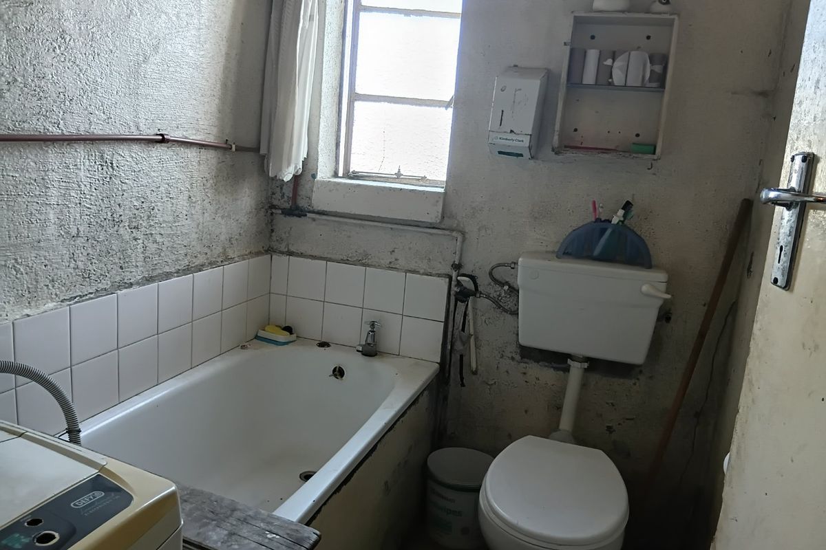 A dated bathroom requiring significant renovation, featuring a bathtub, toilet, and exposed wall surfaces in need of repair and refurbishment.