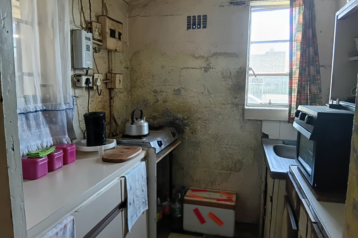 A small, dated kitchen requiring significant renovation, featuring basic cabinetry, a sink, and an oven, with visible wall surface damage.