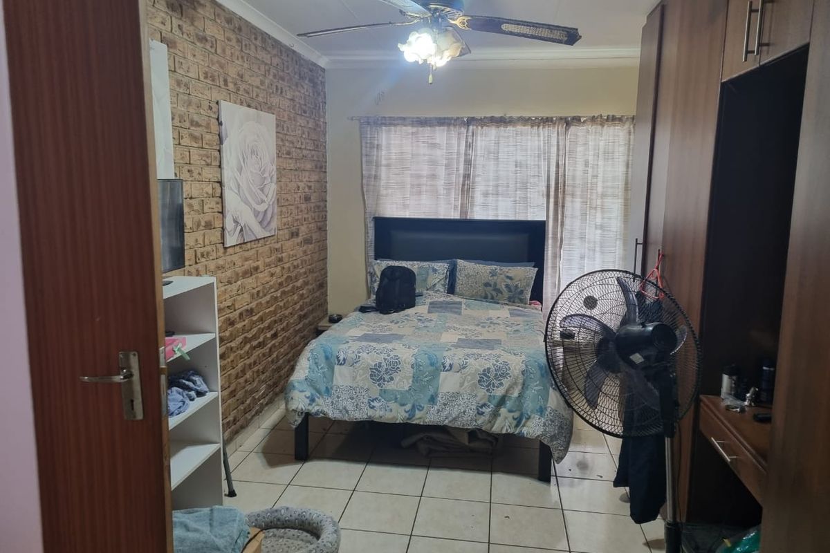 A bedroom featuring an exposed brick feature wall, built-in wooden cupboards, tiled flooring, and a ceiling fan.