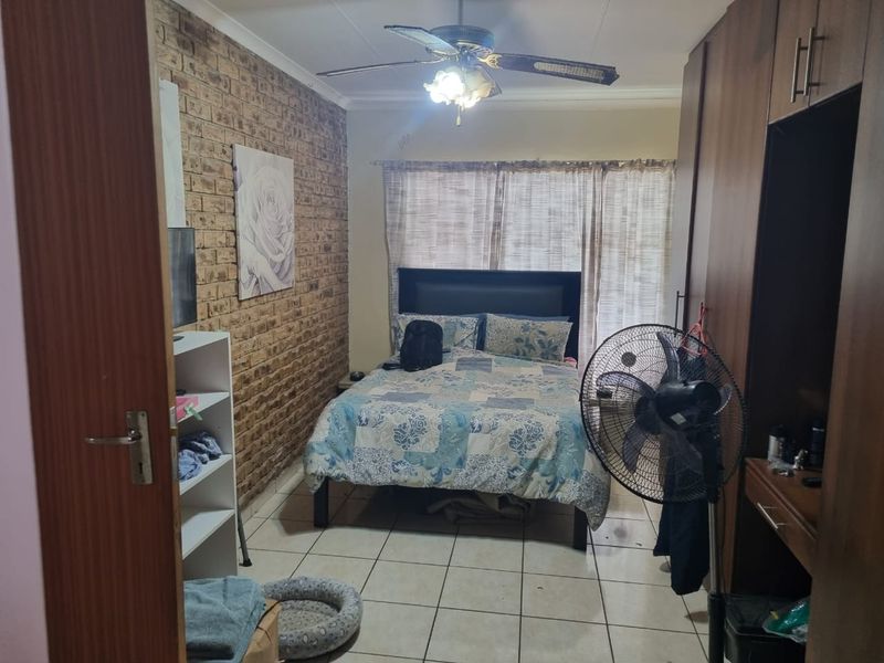 A bedroom featuring an exposed brick feature wall, built-in wooden cupboards, tiled flooring, and a ceiling fan.