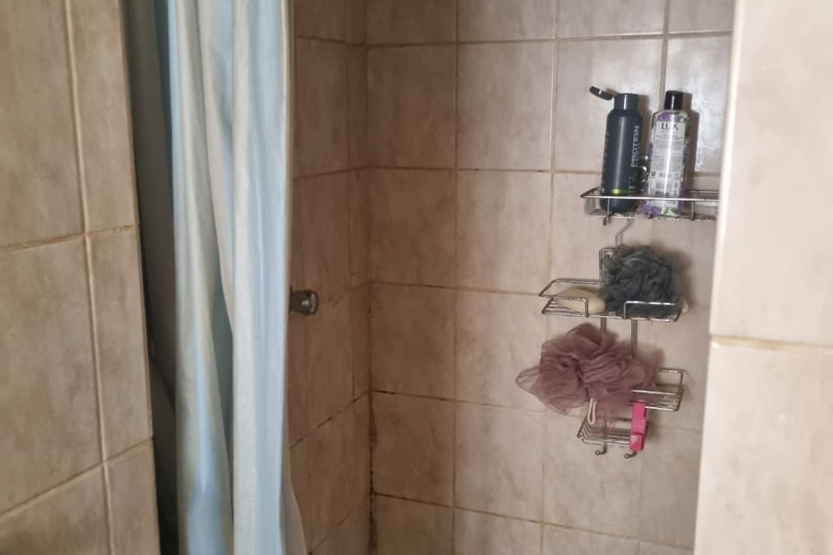 A compact shower stall featuring tiled walls and flooring, equipped with a fixed shower head and curtain.