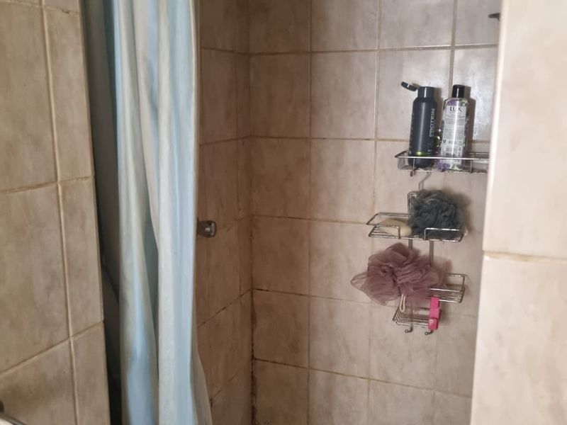 A compact shower stall featuring tiled walls and flooring, equipped with a fixed shower head and curtain.