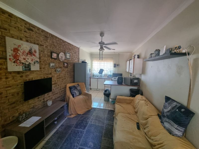 Open-plan living area featuring an exposed brick feature wall, tiled flooring, and a functional kitchen space with built-in cabinetry.