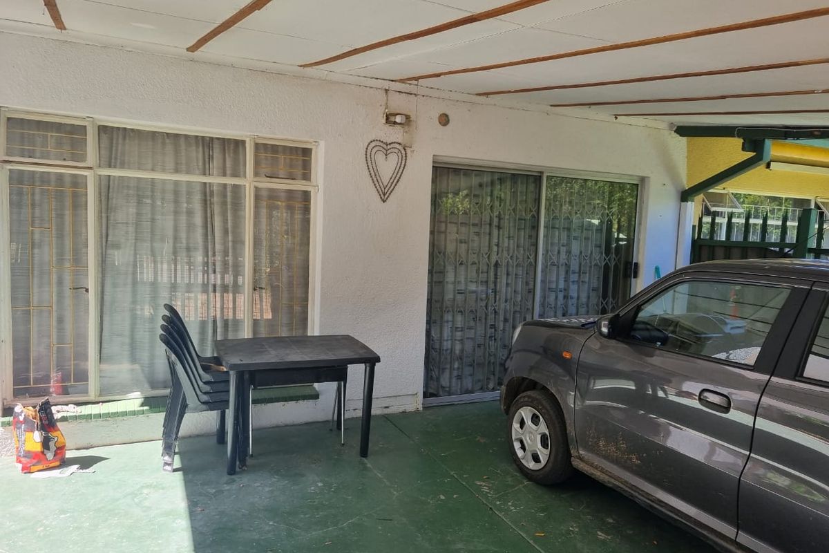 A covered patio area featuring sliding glass doors with security gates and painted concrete flooring, providing a functional outdoor transition space.