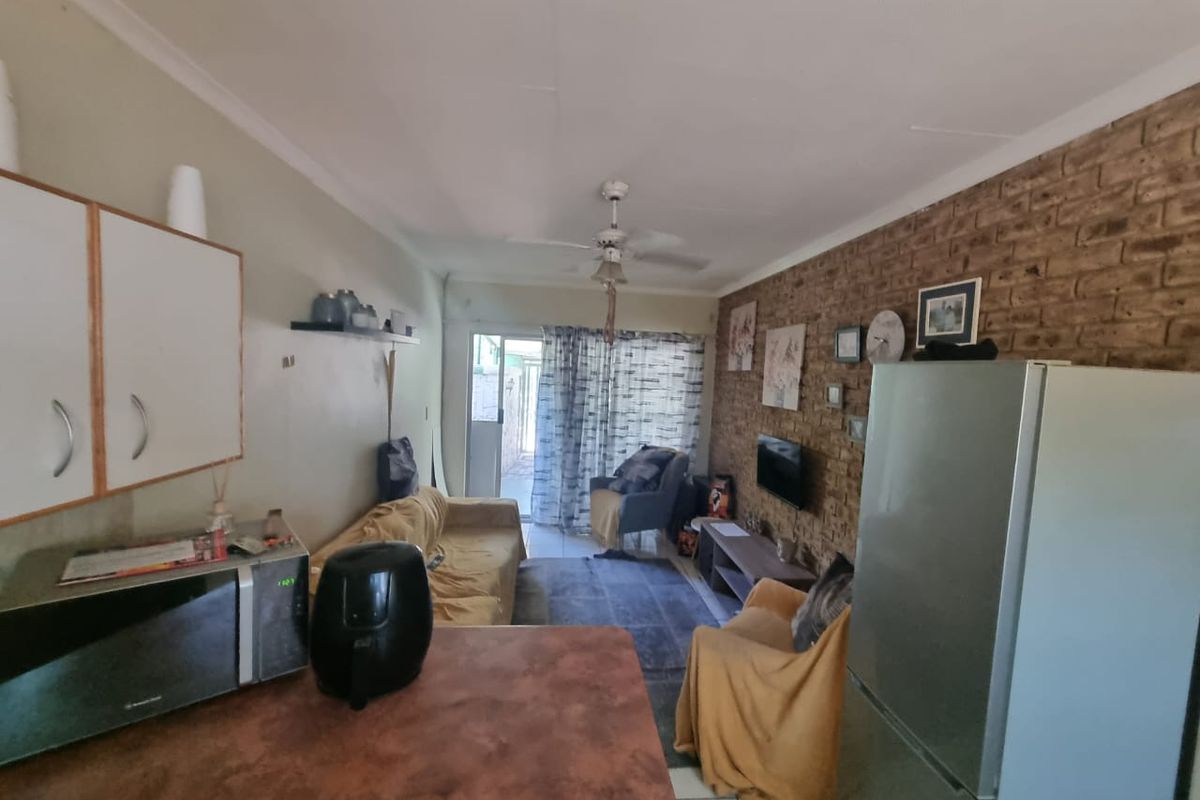 Open-plan living area featuring an exposed brick feature wall, ceiling fan, and kitchen space with built-in cabinetry, leading to an outdoor patio area.
