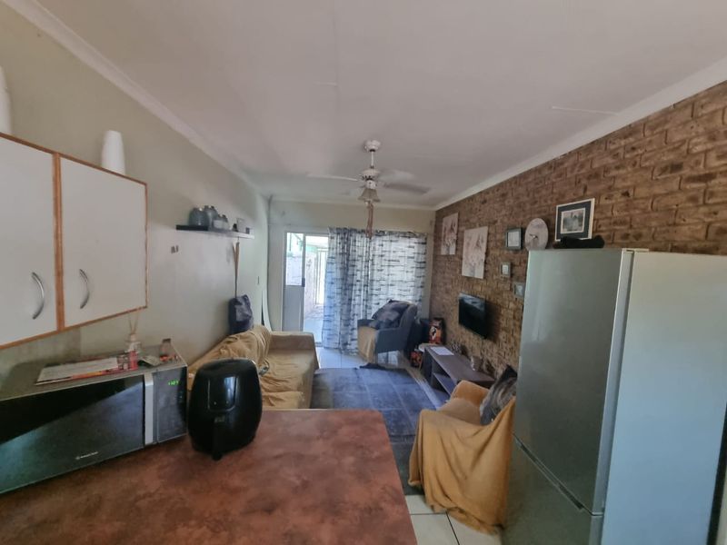 Open-plan living area featuring an exposed brick feature wall, ceiling fan, and kitchen space with built-in cabinetry, leading to an outdoor patio area.