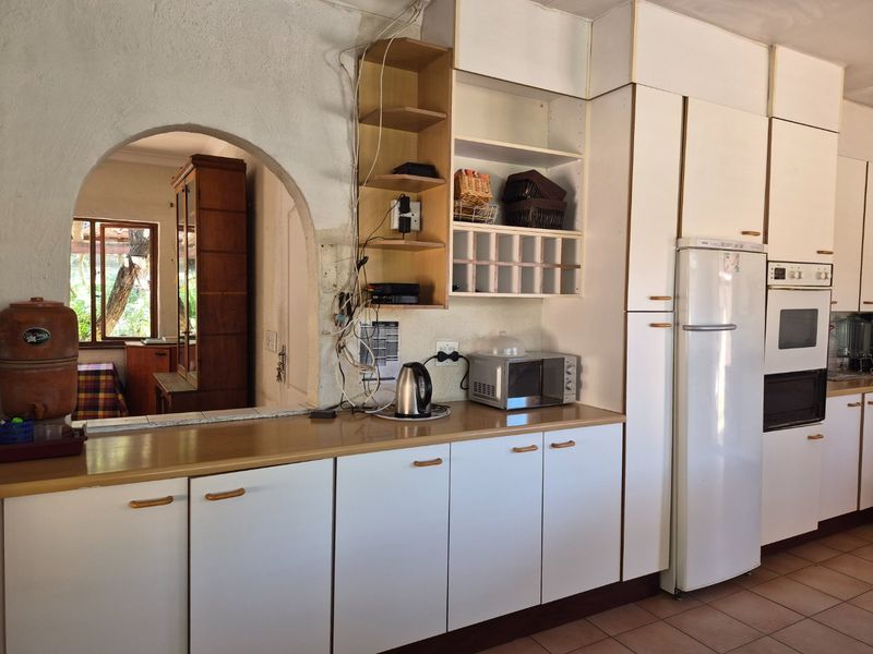 A dated kitchen featuring white cabinetry, laminate countertops, and a distinctive arched opening leading to an adjacent room, with visible exposed electrical wiring.
