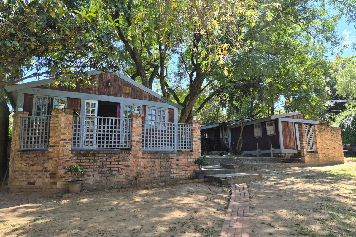 A rustic rear exterior view featuring timber-clad structures with brick foundations, lattice railings, and a brick pathway set within a mature garden.
