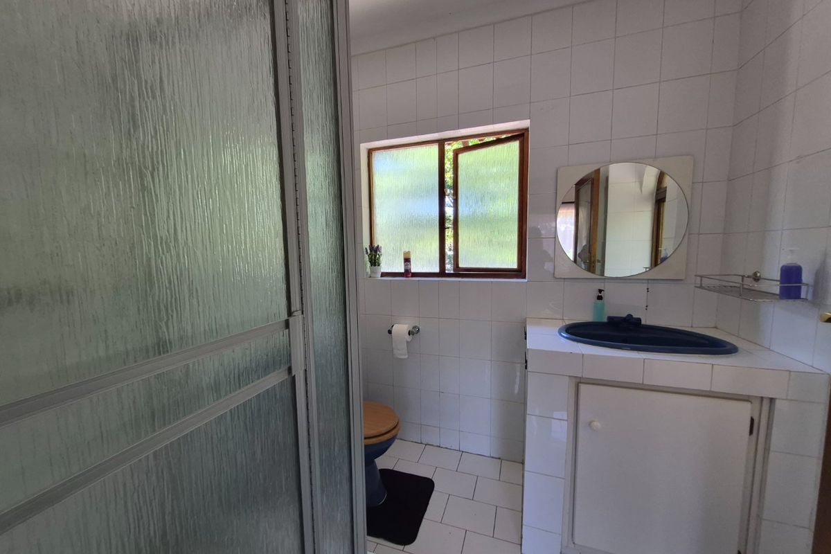 A functional bathroom featuring a shower enclosure, tiled surfaces, and a vanity basin. The space is dated and would benefit from modern updates.