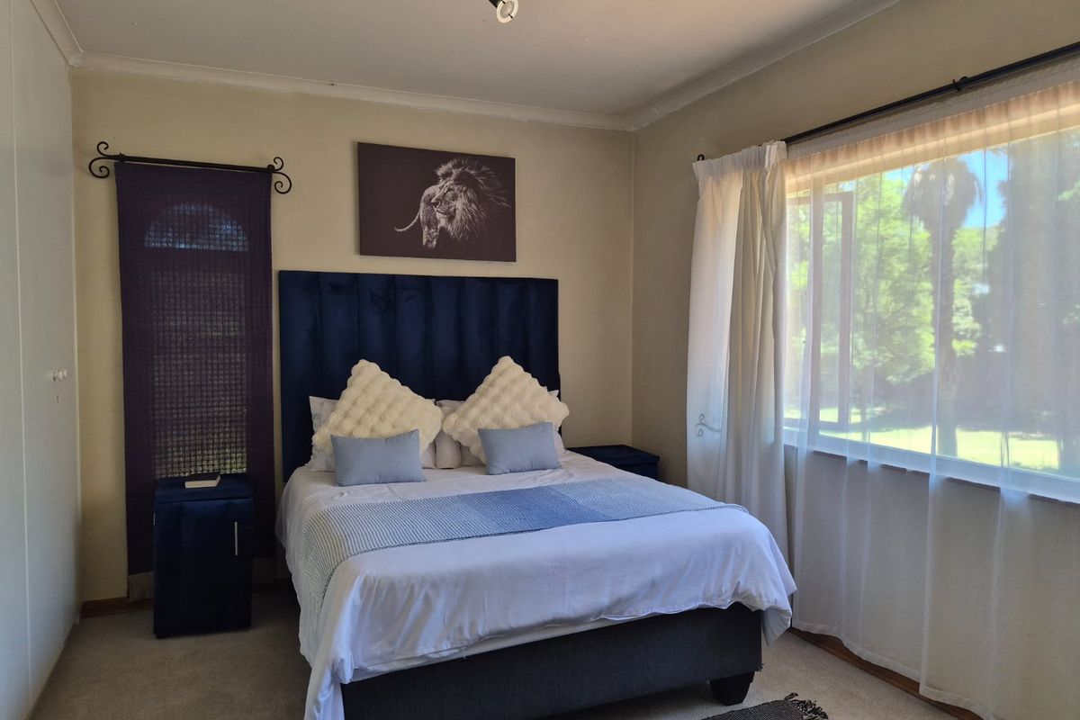 A well-lit bedroom featuring neutral wall finishes, carpeted flooring, and a large window with curtain rails, providing a comfortable and functional living space.