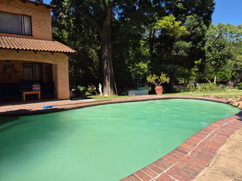 Outdoor pool area featuring a swimming pool with brick coping, adjacent to a covered patio with terracotta roof tiles and mature garden surroundings.