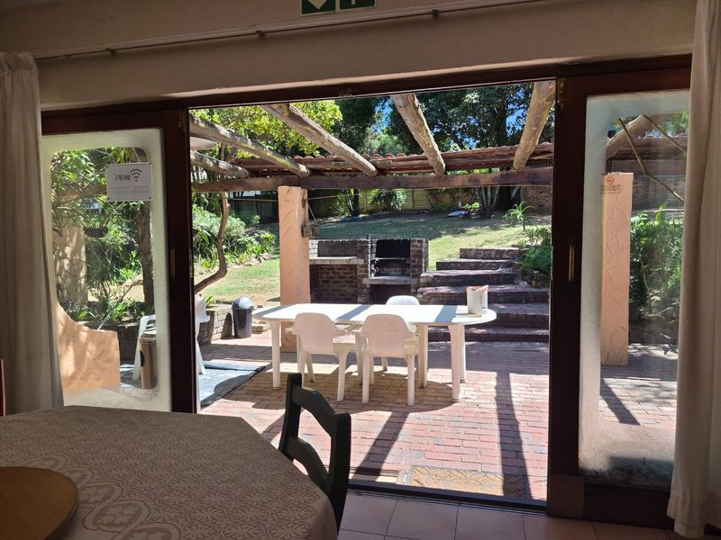 Outdoor patio area featuring a brick built-in braai, timber pergola, and brick paving, accessible through large sliding glass doors.
