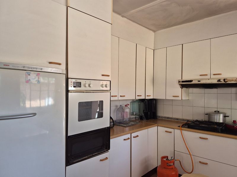A dated kitchen featuring white cabinetry, laminate countertops, a built-in oven, and a gas hob with an extractor fan.