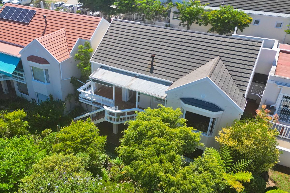 Aerial view of a residential property featuring a tiled roof with solar panels, a raised wooden deck, and a landscaped garden area.