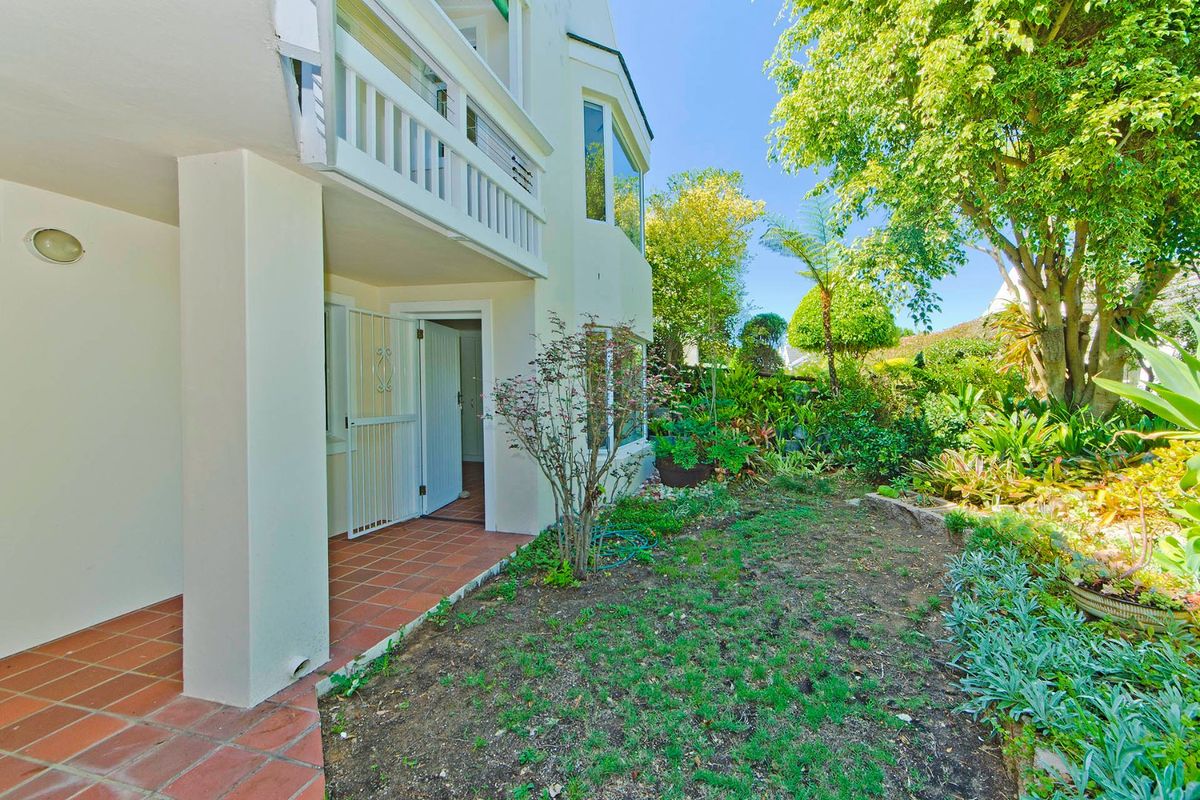 Rear view of the property featuring a covered terracotta tiled patio, a balcony above, and a mature landscaped garden.
