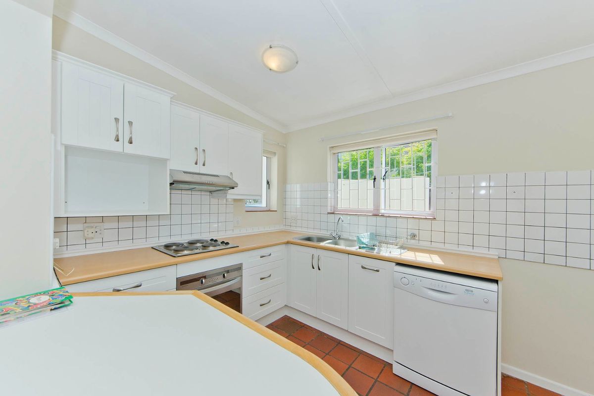 Functional kitchen featuring white cabinetry, laminate countertops, built-in oven, electric hob, extractor fan, and terracotta floor tiles with a tiled backsplash.