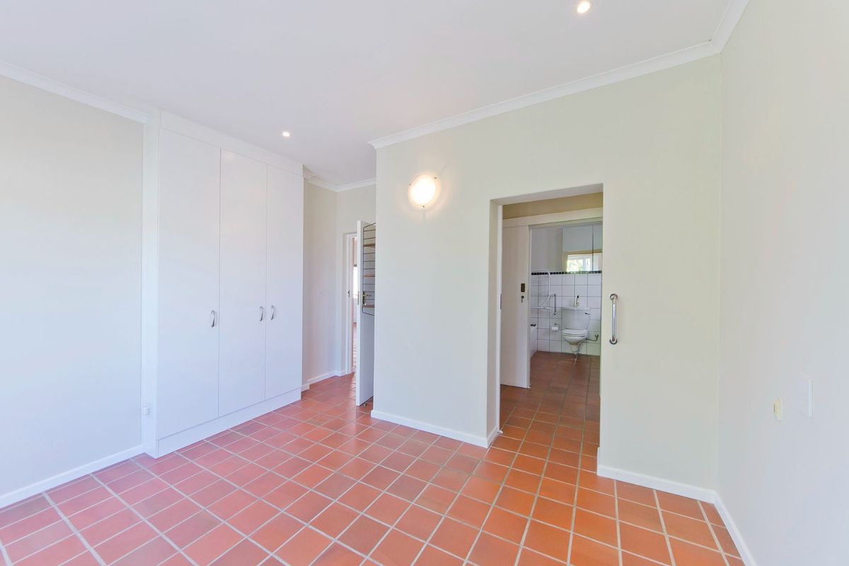 A spacious bedroom featuring built-in cupboards, terracotta floor tiles, and direct access to an en-suite bathroom.