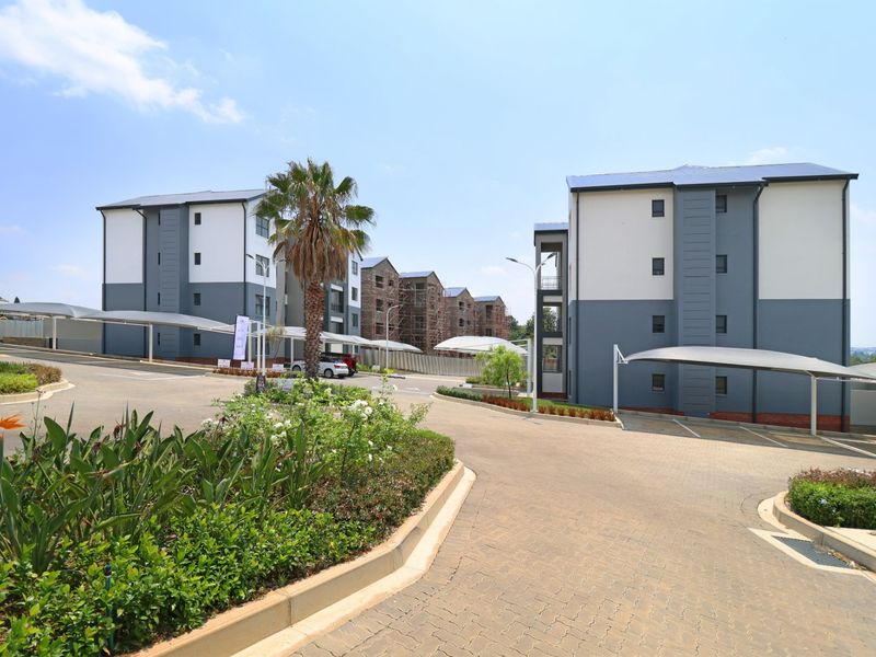 Exterior view of a modern apartment complex featuring paved driveways, covered carport parking, and well-maintained landscaped garden areas.