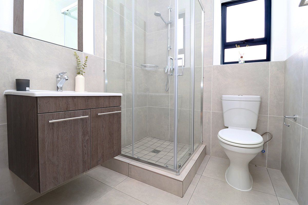 A modern bathroom featuring a floating vanity, a glass-enclosed shower, and a standard toilet with neutral wall and floor tiling.