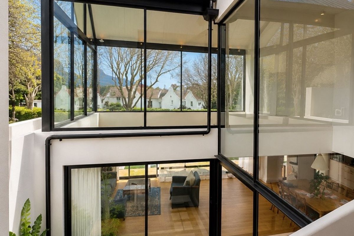 Modern architectural rear elevation featuring extensive floor-to-ceiling glass, black metal framing, and a landscaped courtyard with paved stepping stones.