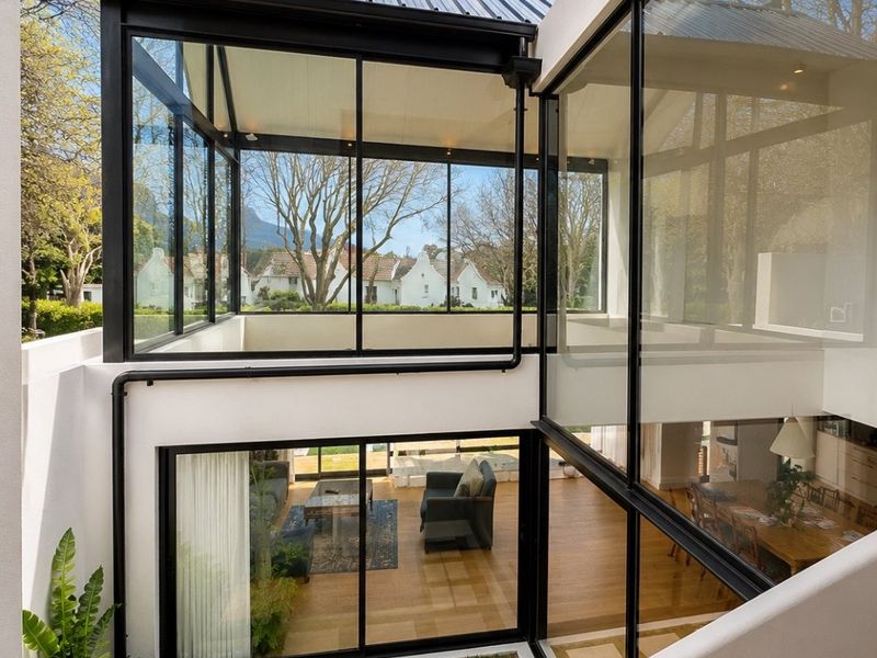 Modern architectural rear elevation featuring extensive floor-to-ceiling glass, black metal framing, and a landscaped courtyard with paved stepping stones.