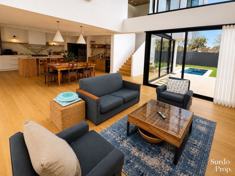 Spacious open-plan living area featuring a modern kitchen, hardwood flooring, and large sliding glass doors that open to a private pool and garden.