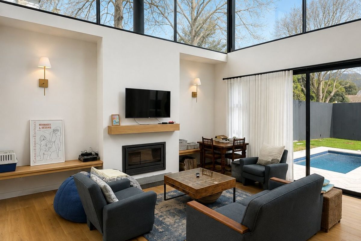 Bright, modern living room featuring high vaulted ceilings, floor-to-ceiling windows, a built-in fireplace, and seamless access to the outdoor pool area.