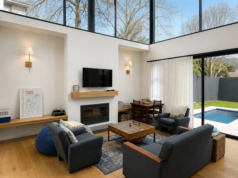 Bright, modern living room featuring high vaulted ceilings, floor-to-ceiling windows, a built-in fireplace, and seamless access to the outdoor pool area.
