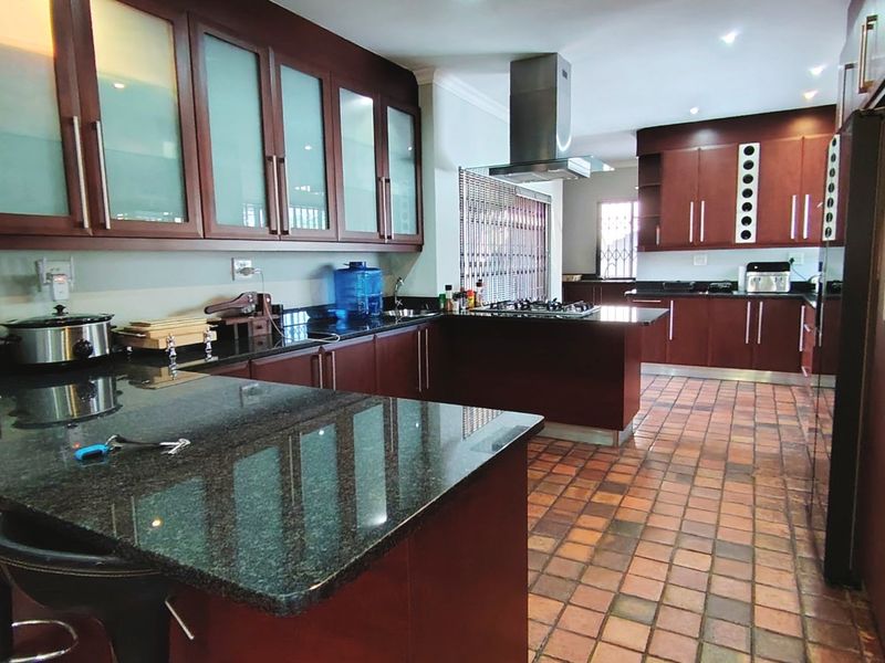 Spacious kitchen featuring dark wood cabinetry, granite countertops, a gas hob with stainless steel extractor, and durable tiled flooring.