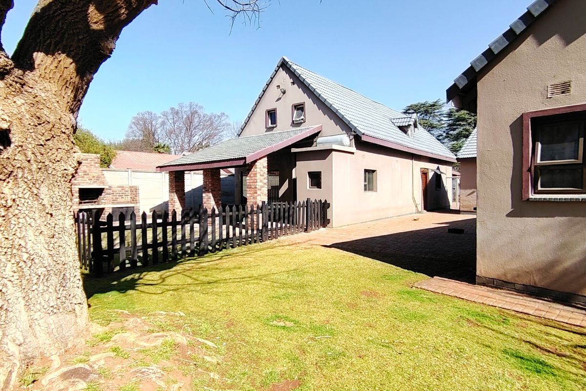 Rear view of the property featuring a paved patio area, a built-in brick braai, and a small garden space enclosed by a picket fence.