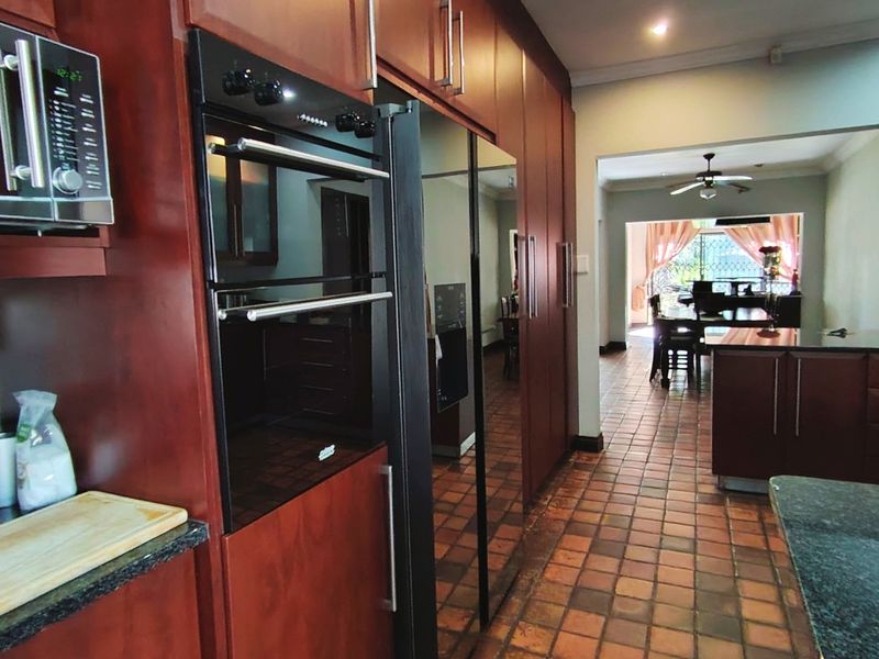 A kitchen featuring dark wood cabinetry, granite countertops, and built-in appliances, with an open-plan layout leading into the dining area.