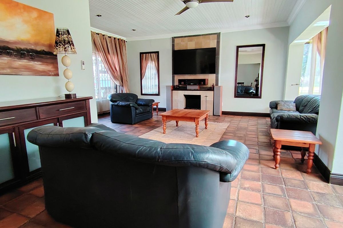 Spacious living room featuring terracotta tiled flooring, a central fireplace with a tiled surround, and a classic beadboard ceiling with a fan.