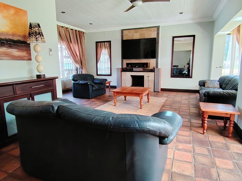 Spacious living room featuring terracotta tiled flooring, a central fireplace with a tiled surround, and a classic beadboard ceiling with a fan.
