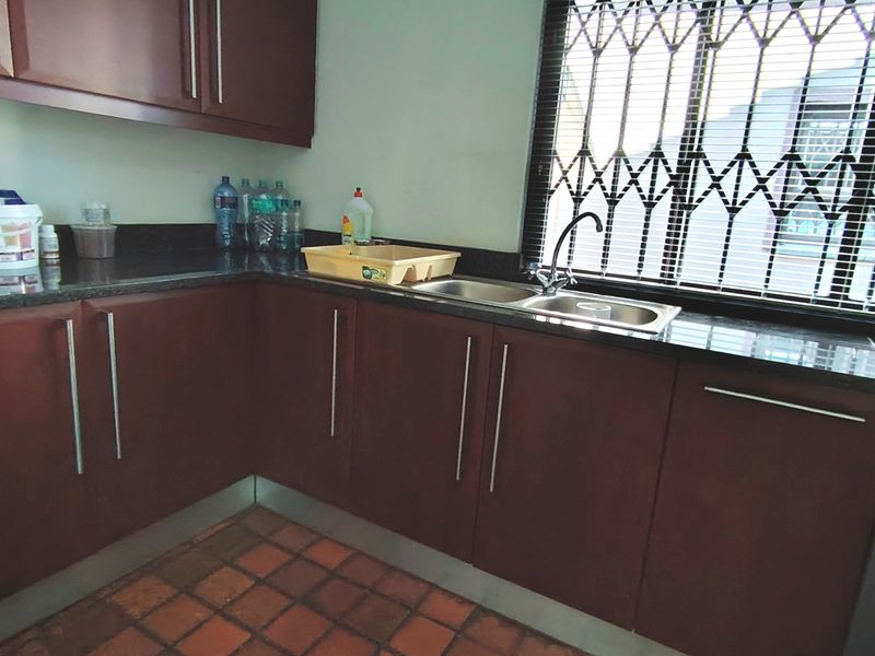 A functional kitchen featuring dark wood cabinetry, granite countertops, a double basin sink, and tiled flooring with a window security gate.