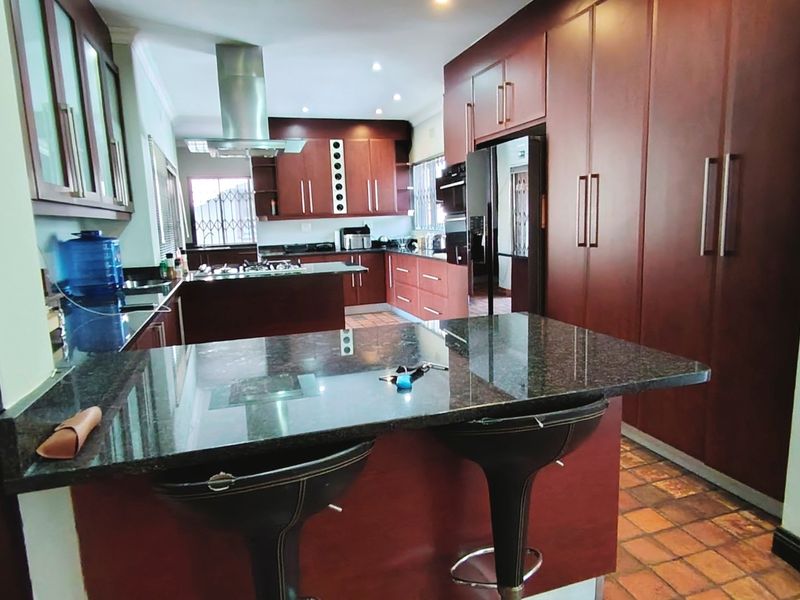 Spacious kitchen featuring dark wood cabinetry, granite countertops, built-in appliances, and terracotta tile flooring with a central breakfast bar.