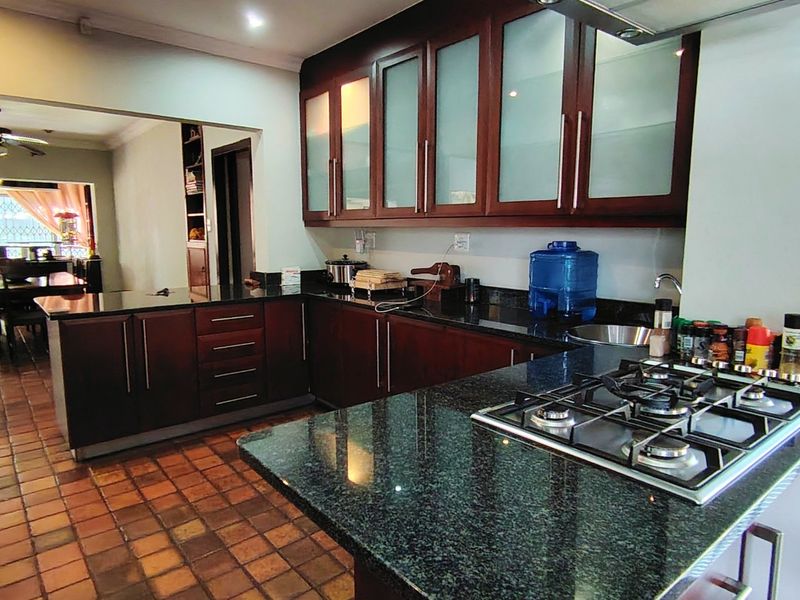 A functional kitchen featuring dark wood cabinetry, granite countertops, a built-in gas hob with extractor, and traditional terracotta floor tiles.