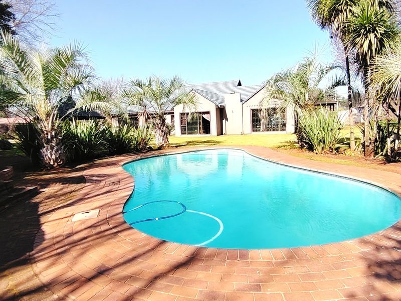A well-maintained swimming pool set within a landscaped garden, featuring brick paving surrounds and a view of the rear house elevation.