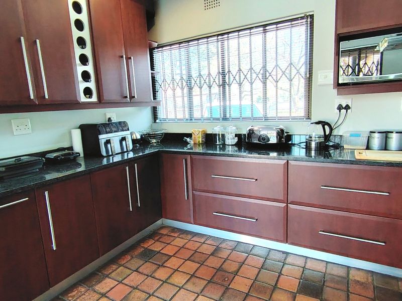 A functional kitchen featuring dark wood cabinetry, granite countertops, a built-in microwave, and a window with security bars.
