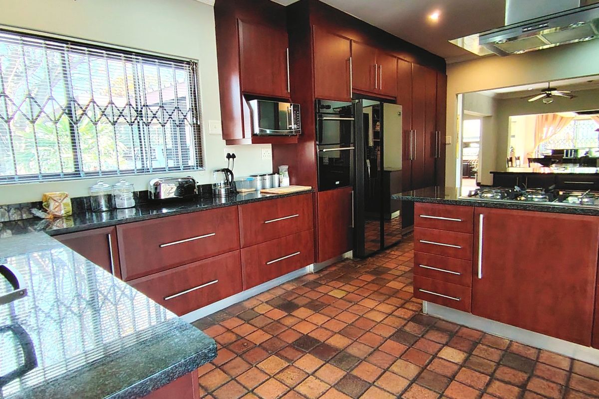 Spacious kitchen featuring dark wood cabinetry, granite countertops, built-in appliances, and a gas hob, with terracotta floor tiles and a window security gate.