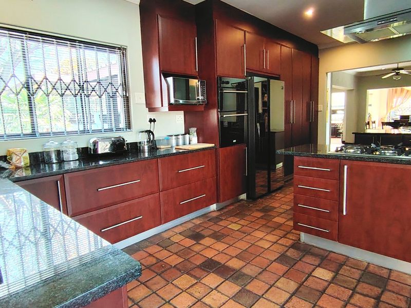 Spacious kitchen featuring dark wood cabinetry, granite countertops, built-in appliances, and a gas hob, with terracotta floor tiles and a window security gate.