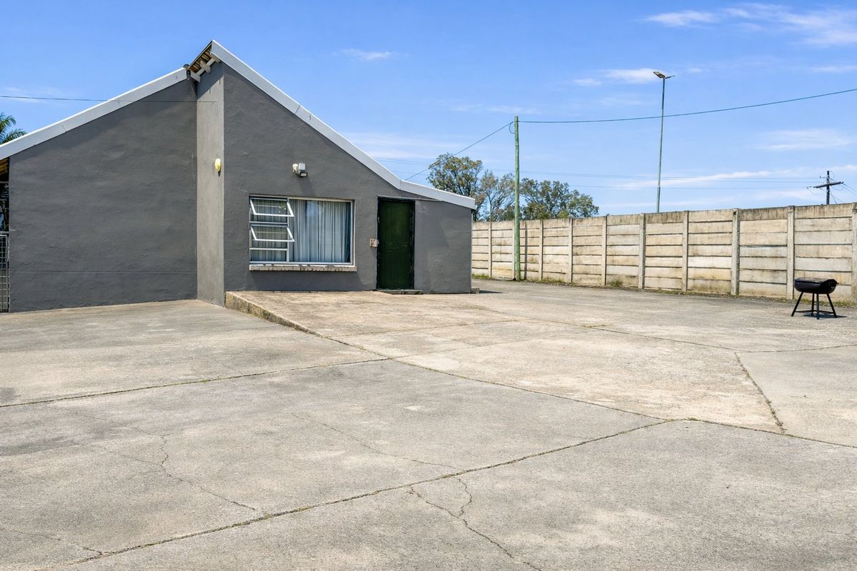 Rear exterior view of the property featuring a large concrete paved area and a precast concrete boundary wall.