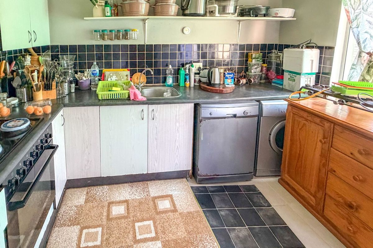 A functional kitchen featuring a built-in oven, hob, extractor fan, stainless steel sink, and tiled backsplash with ample storage cabinetry.