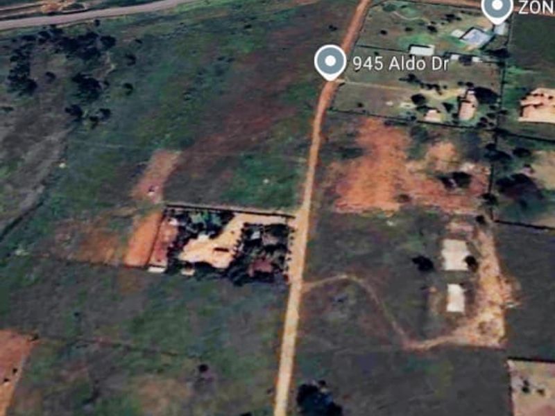 An aerial view of a vacant residential land parcel with dirt road access and surrounding rural landscape.