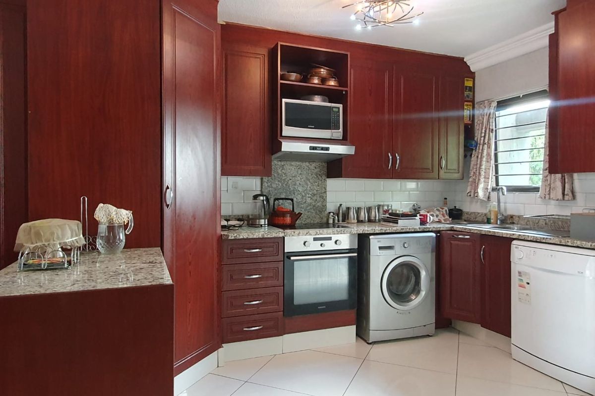A functional kitchen featuring dark wood cabinetry, granite countertops, subway tile backsplash, and integrated appliances including an oven and extractor fan.