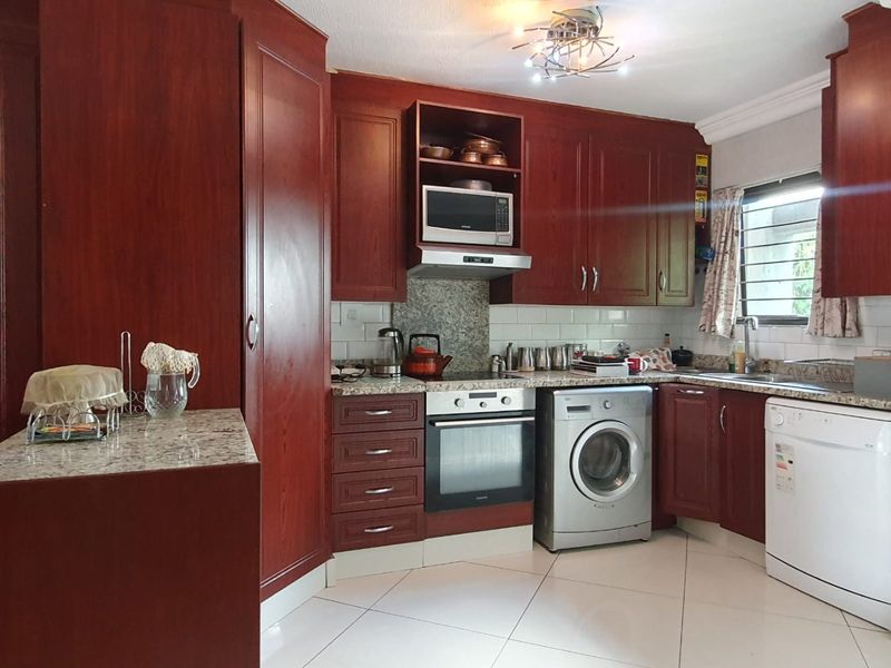 A functional kitchen featuring dark wood cabinetry, granite countertops, subway tile backsplash, and integrated appliances including an oven and extractor fan.