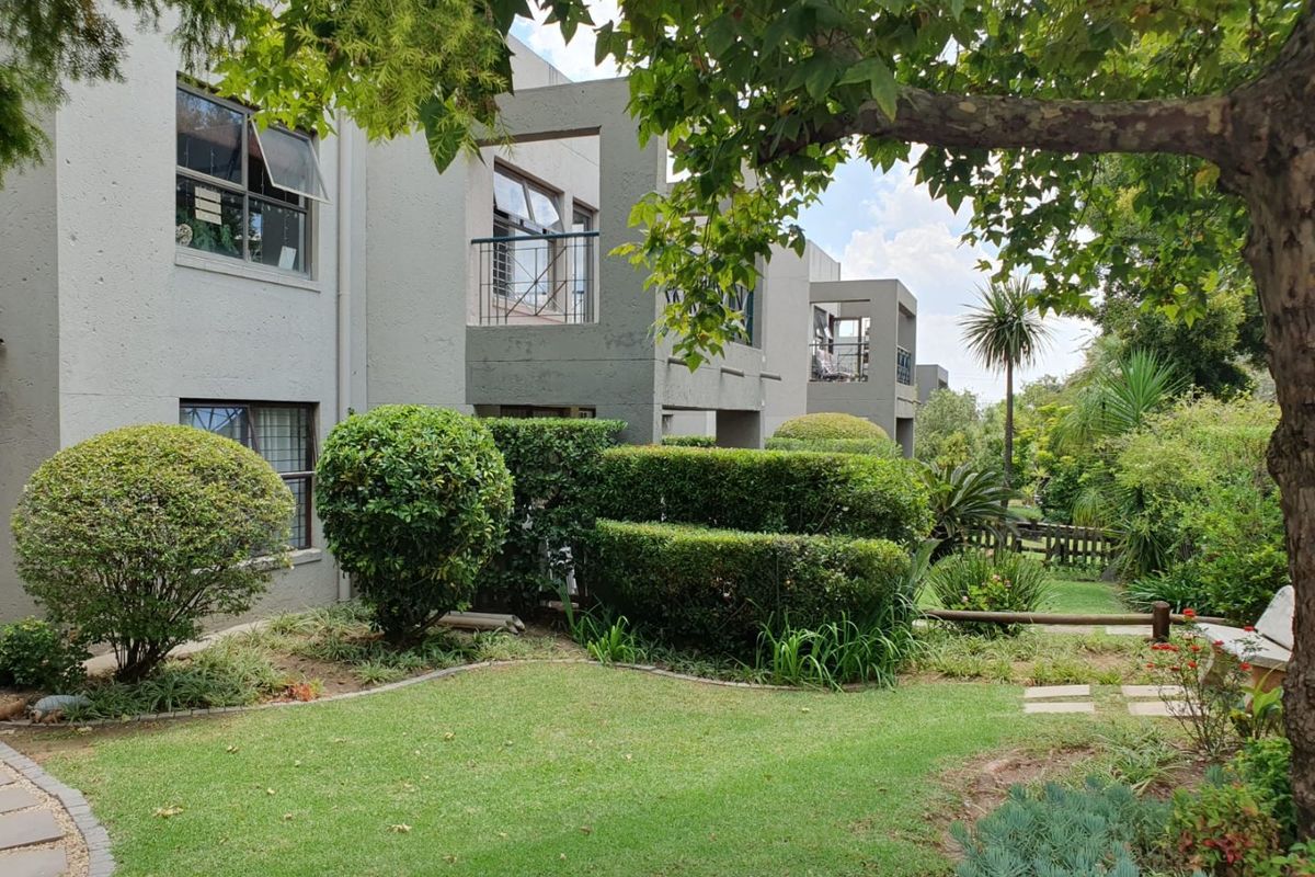 A view of the apartment complex rear elevation featuring private balconies, well-maintained landscaped gardens, and paved pathways.