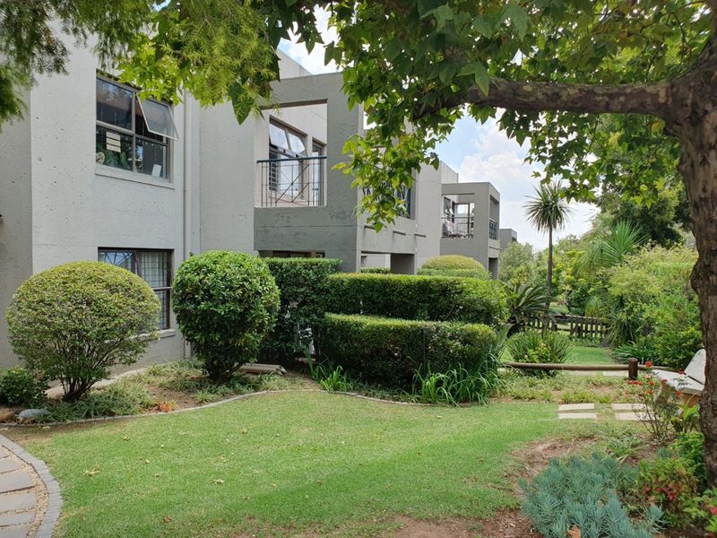 A view of the apartment complex rear elevation featuring private balconies, well-maintained landscaped gardens, and paved pathways.