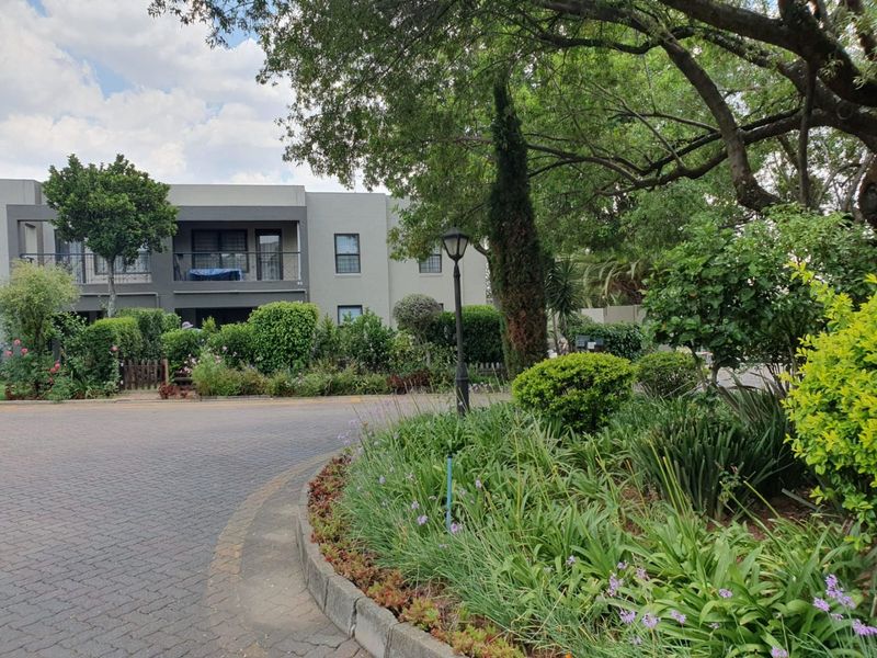 A view of the apartment complex exterior featuring a well-maintained landscaped garden, paved driveway, and balcony access.